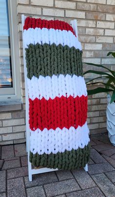 a large knitted blanket sitting on top of a white chair next to a brick wall