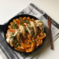 a skillet filled with pasta and meat covered in sauce next to a pair of chopsticks