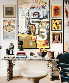 a living room filled with lots of art on the wall above a glass top table