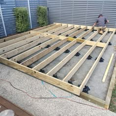 a man working on building a deck in the backyard with wood framing and concrete flooring