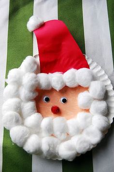 a paper plate with a santa hat on it and eyes in the center, sitting on a green striped pillow