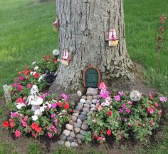 there is a fairy door in the middle of some flowers and rocks near a tree