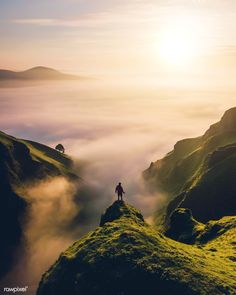 a person standing on top of a lush green hill covered in fog and mist under a bright sun