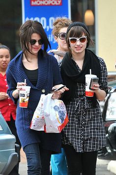 two girls walking down the street with drinks in their hands and cell phones in their hand