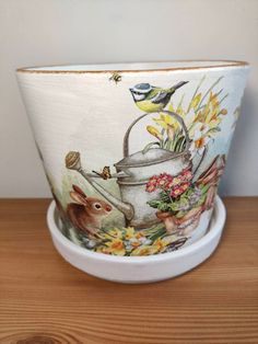 a pot with flowers and birds painted on it sitting on top of a wooden table