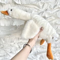 a hand holding a stuffed duck on top of a white bed sheet with ruffles