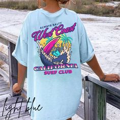 California surf T-shirt. Skeleton surfing on the back with a small pocket design in front. Perfect tee to wear this summer or all year round. Perfectly preppy attire. To wear this oversized, size up 1-2 sizes. *Unisex sizing. Please see size chart in photos*  No side seams mean there are no itchy interruptions under the arms. The shoulders have tape for improved durability. .: 100% cotton (fiber content may vary for different colors) .: Medium fabric (5.3 oz/yd² (180 g/m .: Classic fit .: Tear-away label .: Runs true to size Blue Beach T-shirt With Front Print, Blue T-shirt With Front Print For Beach, Blue Summer T-shirt For Surfing, Summer Surfing Vsco T-shirt, Summer Letter Print Tops For Streetwear, Blue Tops For Streetwear And Beach Season, Blue Beach Top With Front Print, Casual Blue T-shirt With Back Print, Trendy Cotton T-shirt For Surfing