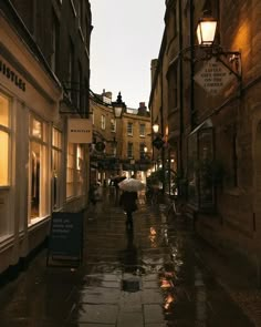 a person holding an umbrella walking down a wet street in the rain with buildings on both sides