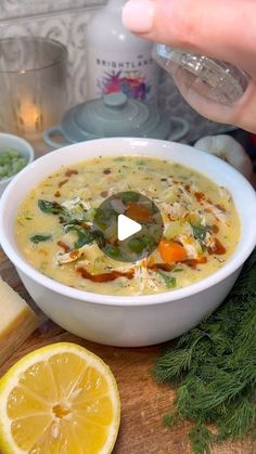 a bowl of soup on a wooden table with lemons and other ingredients around it