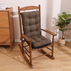 a wooden rocking chair in a room with a plant on the floor next to it