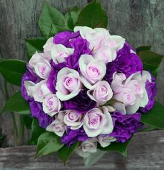 a bouquet of purple and white flowers sitting on top of a wooden bench