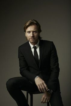 a man in a suit and tie sitting on a stool