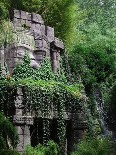 a stone statue with vines growing on it's face next to a small waterfall