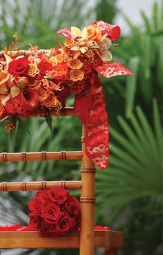 an arrangement of red and orange flowers on a bamboo chair with ribbon tied around it