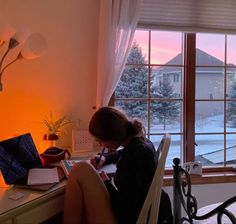 a woman sitting at a desk with a laptop and pen in front of her, looking out the window