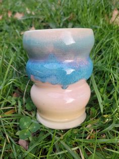 three vases sitting in the grass on top of each other, one blue and one pink