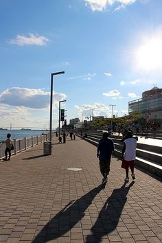 two people walking down a sidewalk next to the ocean