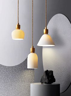 three white lamps hanging from gold chains in front of a mirror and black rock on a pedestal