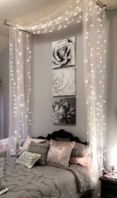 a bedroom with lights strung from the ceiling and a bed covered in grey sheets, pillows and blankets