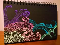 a black notebook with colorful swirls on it sitting on top of a wooden table