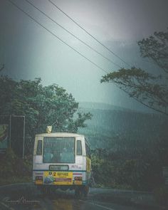 a bus driving down the road in the rain with trees and hills in the background