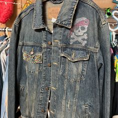 a denim jacket with patches and skulls on the back is hanging in front of clothes