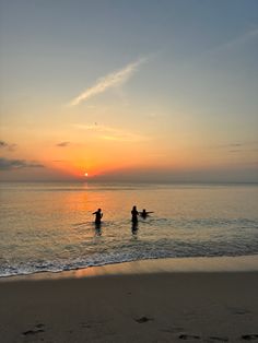 two people standing in the ocean at sunset