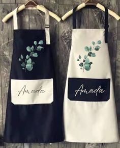 two personalized aprons are hanging on a wooden wall, one with an embroidered flower and the other with leaves