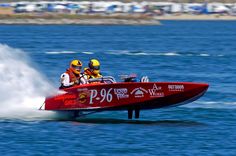 two men riding on the back of a red speed boat