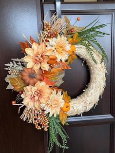 a wreath is hanging on the front door with autumn leaves and flowers around it,