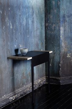 a black table with a bowl on it in front of a blue wall and wooden floor