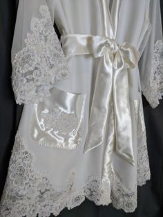 the robe is white with lace on it and has a satin sash around its waist