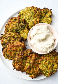 a white plate topped with broccoli patties next to a bowl of sour cream