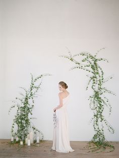 a woman in a white dress standing next to some plants and candles on the floor