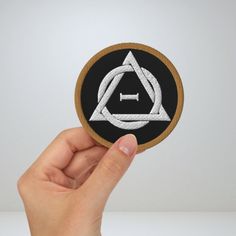 a hand is holding up a patch with an image of a triangle in the center