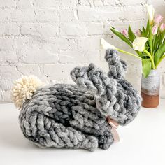 a gray knitted bunny sitting next to a vase with tulips