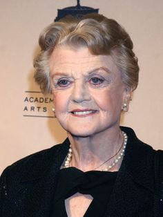 an older woman wearing a black jacket and pearls on her neck posing for the camera