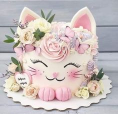 a white cake decorated with pink flowers and a cat's face on top of it