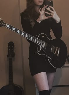 a woman holding a guitar and taking a selfie with her cell phone in front of her