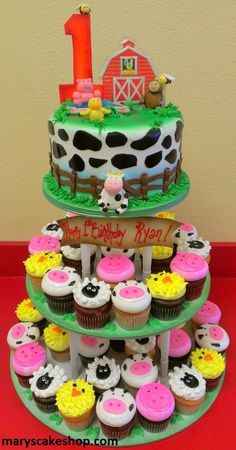 two tiered cake with cupcakes and farm animals on the top one is for 1st birthday