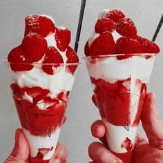 two ice cream sundaes with raspberries in them are being held up