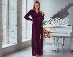 a woman standing in front of a grand piano wearing a purple velvet dress with thigh high slit