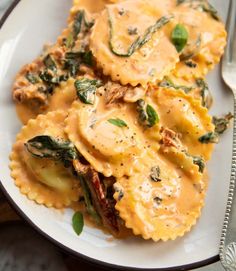 a white plate topped with ravioli and spinach covered in cheese sauce next to a fork