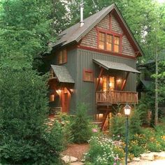 a house in the woods surrounded by trees and flowers with lights on at the front