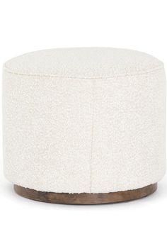 a white ottoman with wood legs and fabric upholstered on the top, in front of