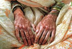 two hands covered in henna on top of a bed with orange and white sheets