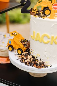 a birthday cake with construction trucks on top and decorations around the base that says jack