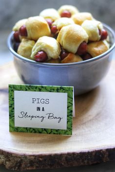 a metal bowl filled with pigs in a blanket sitting on top of a wooden table