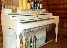 a white piano with wine glasses and bottles on it in front of a wooden wall