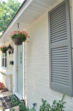 a white house with grey shutters and flower pots on the front door window sill